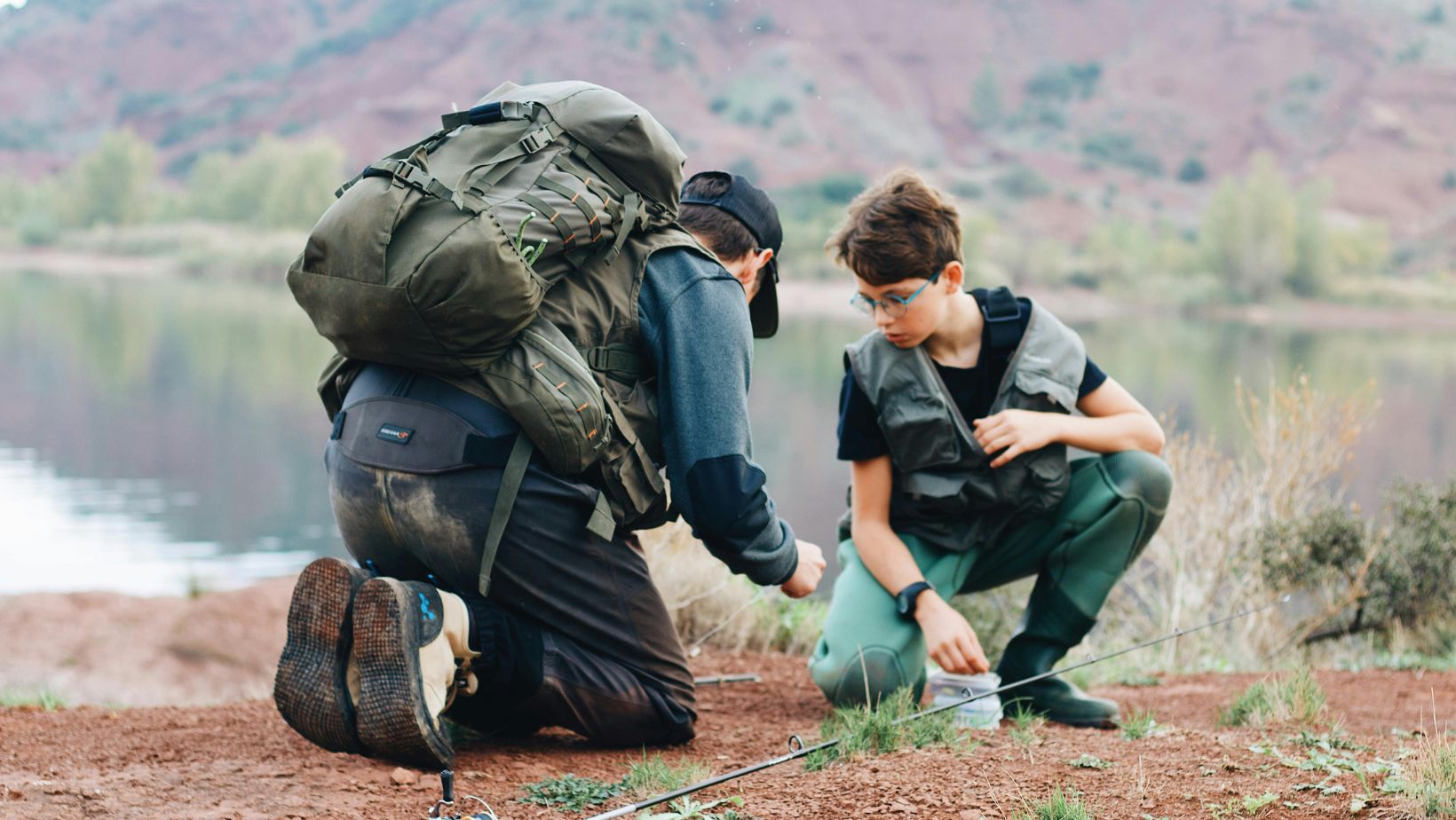 man kneeling on ground beside boy with fishing gear